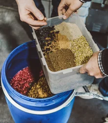 Hands pouring foraged botanicals from a box into a blue barrel