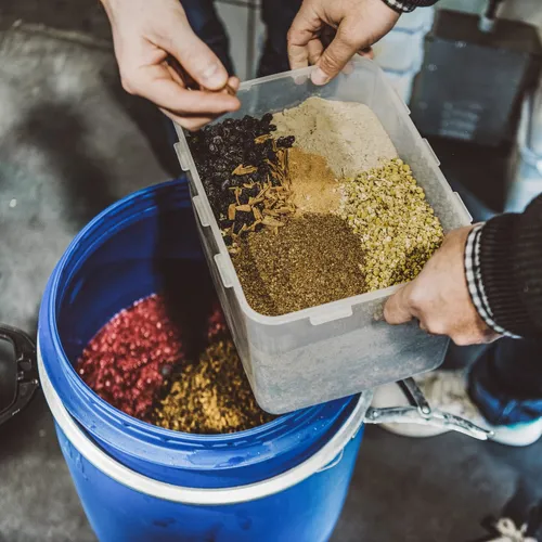 Hands pouring foraged botanicals from a box into a blue barrel
