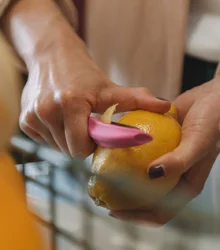 Hands peeling an orange with a peeler