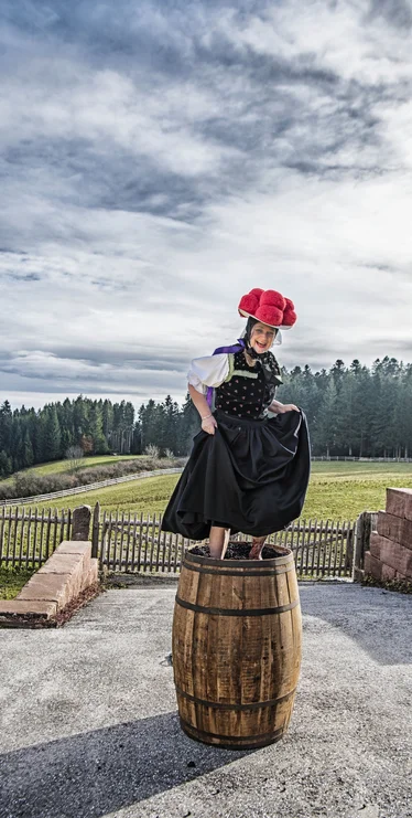 Woman in Black Forest traditional dress with Bollenhut standing on a barrel