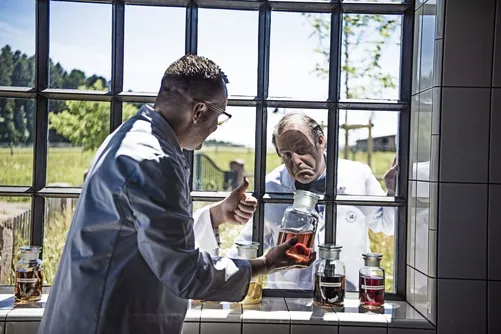 Man in lab coat inspecting a jar by the window