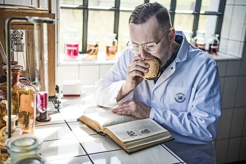 Man in lab coat smelling a jar while reading