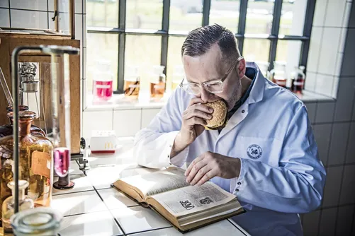 Man in lab coat tasting from a jar over an open book