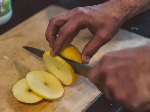 Hands slicing apple rings on a cutting board