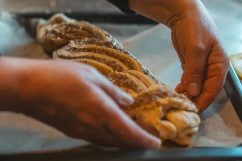 Hands shaping a braided hazelnut yeast loaf on baking paper