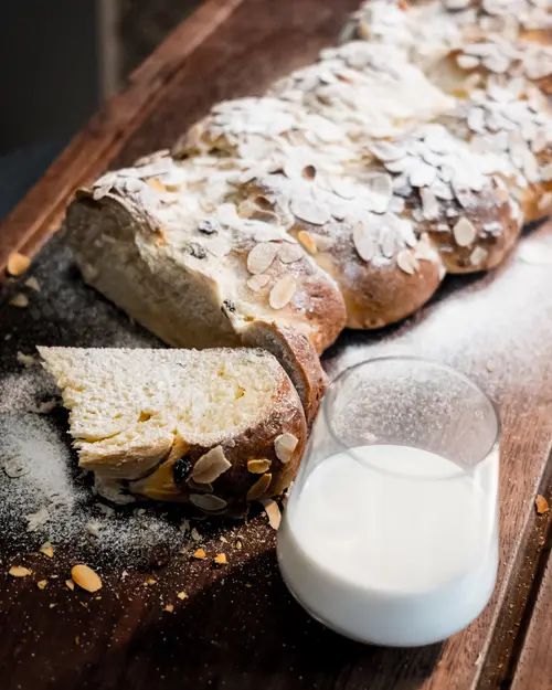 Sliced yeast plait dusted with sugar next to a glass of milk