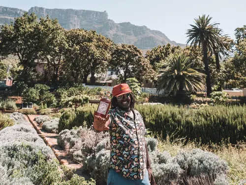 Man holding a Monkey 47 bottle in a garden with Table Mountain behind