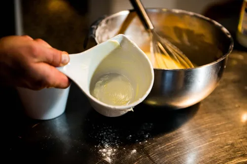 Pouring cream into a bowl of egg mixture