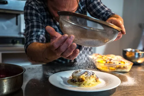 Dusting a dessert with icing sugar through a sieve