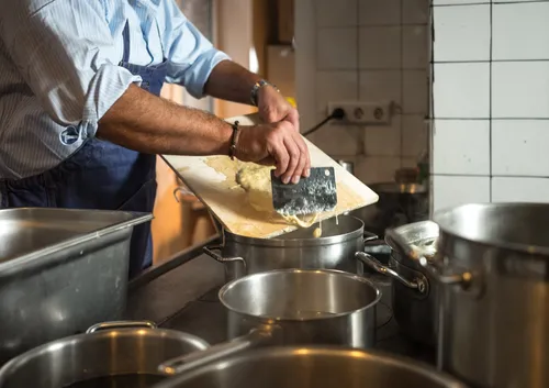 Chef scraping Spätzle into a pot of boiling water