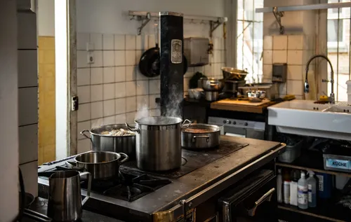 Steaming pots on a stove in a tiled restaurant kitchen