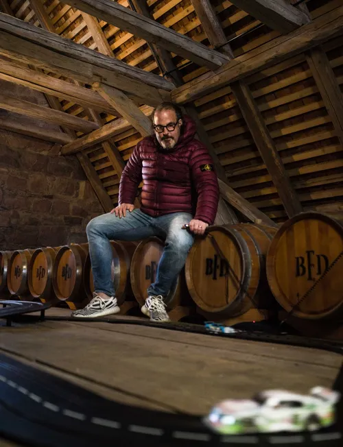 Man sitting on an oak barrel next to a toy race track