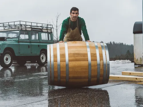 Distiller rolling an oak barrel beside a vintage Land Rover