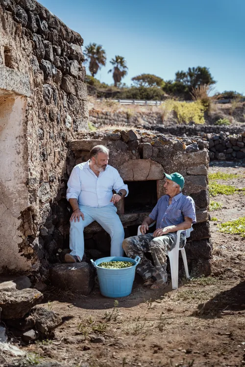 Two caper farmers sitting in a stone doorway