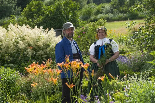 Two people in a flowering Black Forest garden, one in traditional costume