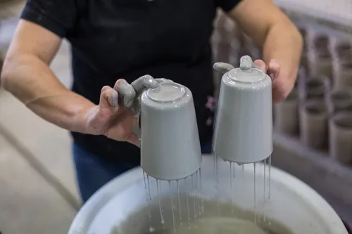 Hands dipping stoneware Becher cups into glaze