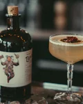 Dresdner Allerlei cocktail in a coupe next to an illustrated gin bottle