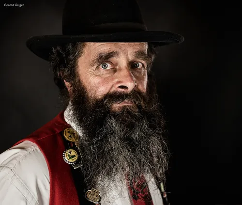 Man with a dark full beard and black hat in traditional costume