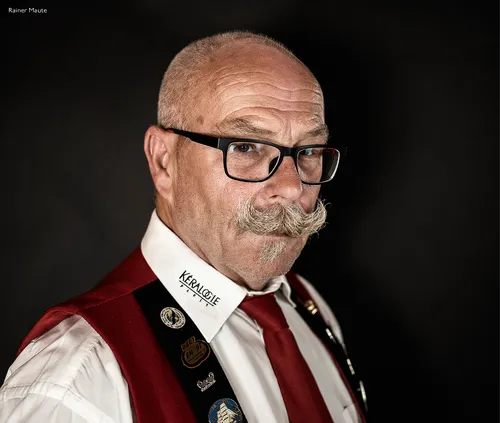 Man with glasses and a waxed moustache in a club waistcoat with badges