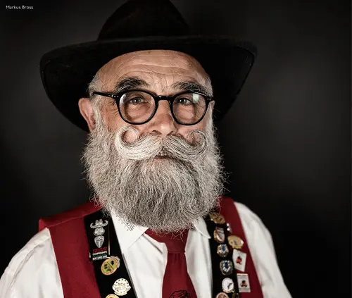 Bearded man with glasses and a black hat in traditional costume with badges