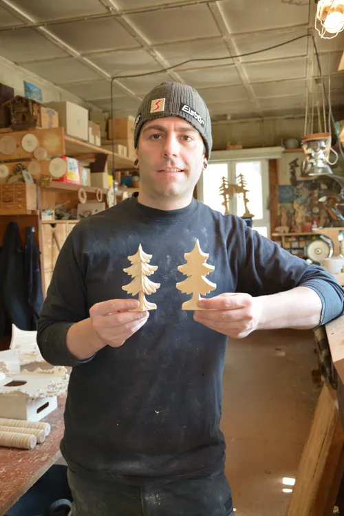 Cuckoo clock maker holding two carved wooden fir tree pieces
