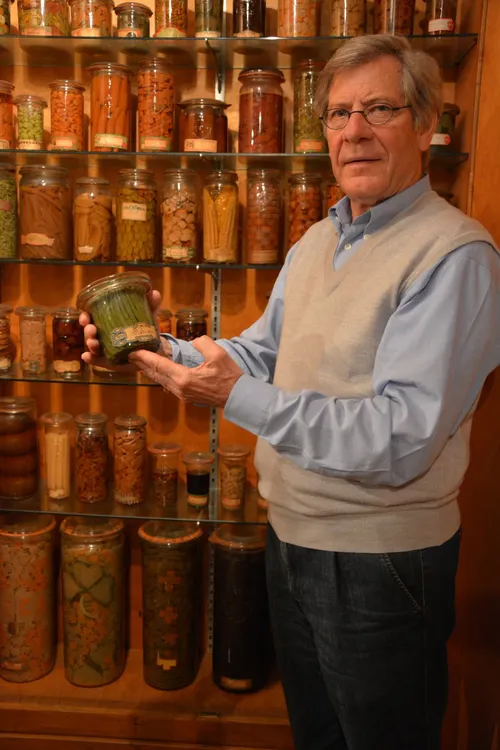 Man holding a preserving jar in front of shelves of jars