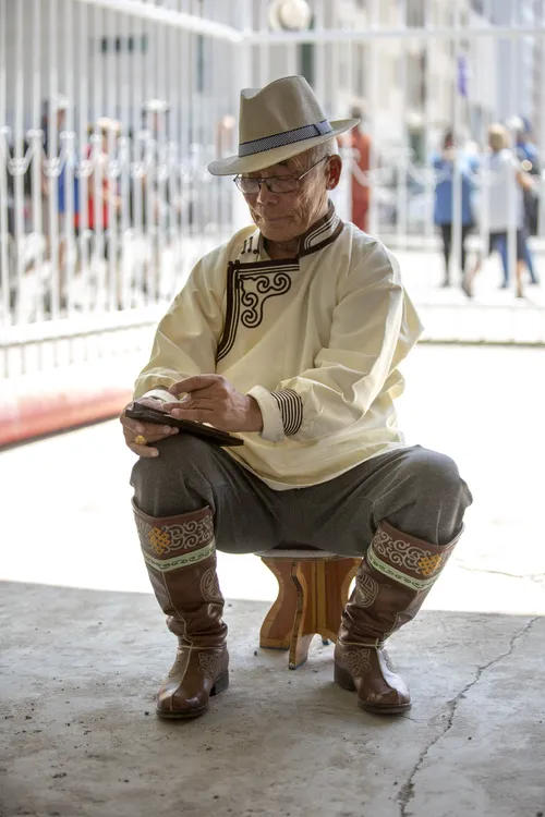 Man in a traditional Mongolian robe crouching and writing