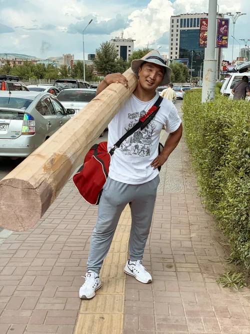 Man carrying a large wooden pole on a city sidewalk