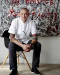 Chef in whites seated on a chair in front of a painted wall