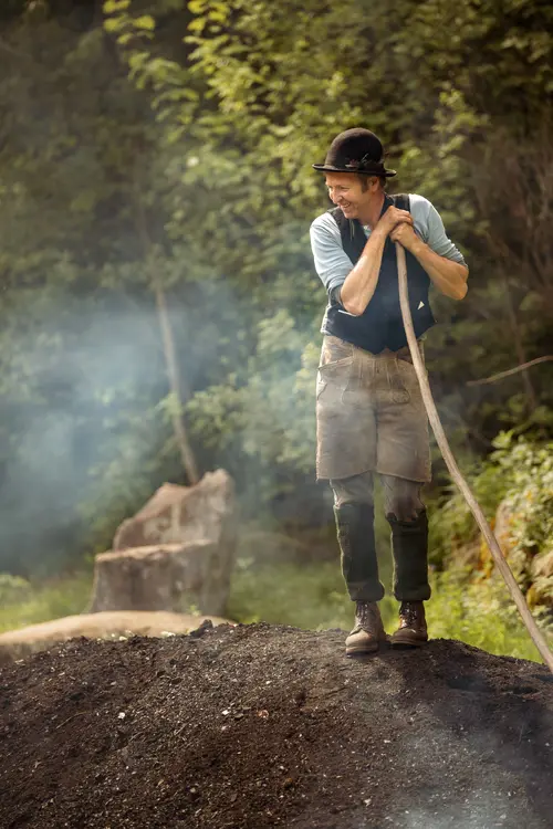 Charcoal burner tending a smoking charcoal kiln