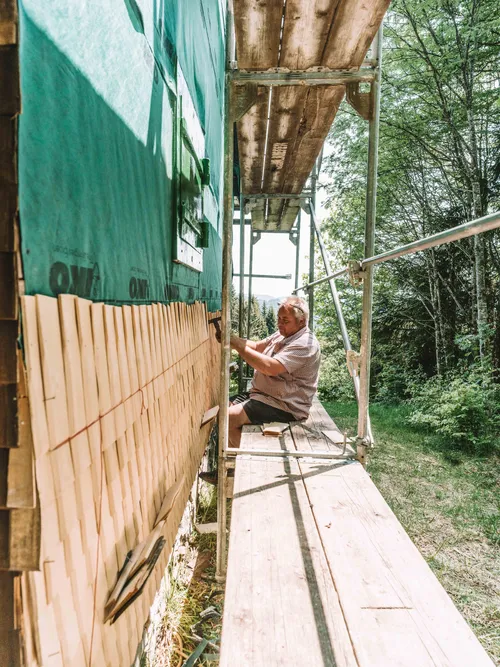 Roofer nailing wooden shingles onto a house wall from scaffolding